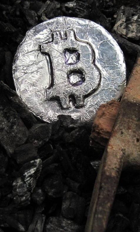 Picareta ao lado de moeda de prata com símbolo do BItcoin no centro
